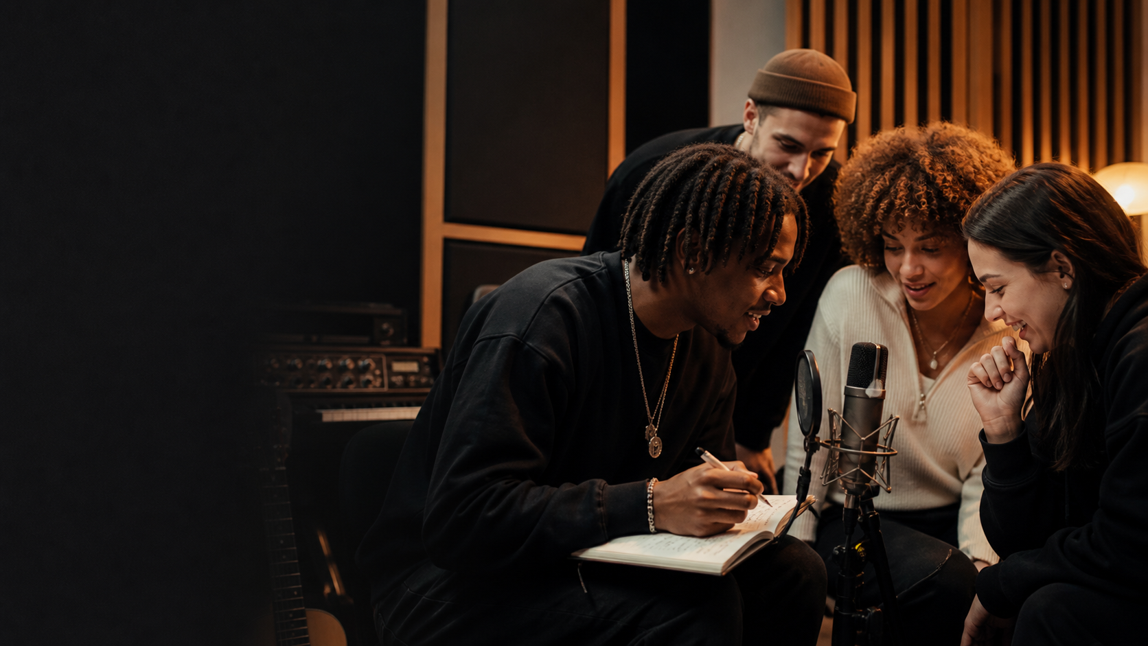Un grupo comparte ideas y escribe junto a un micrófono en un estudio de música.